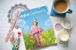 Caboodle Magazine flatlay of front cover with tea, candle, nail polish and hand cream